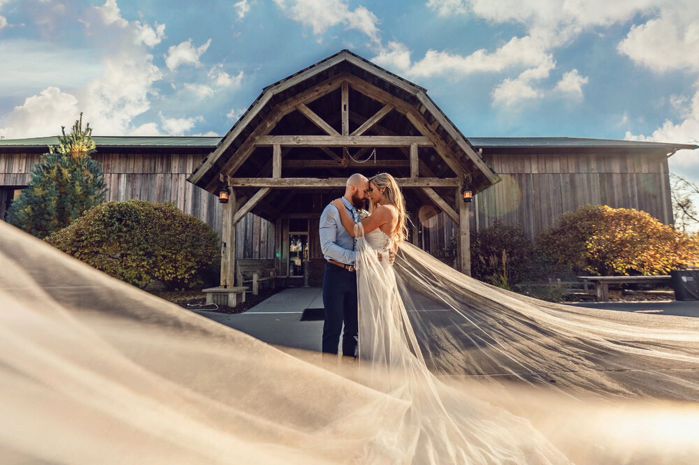 bride with flowing dress get photographed in front of a barn at their wedding in iowa