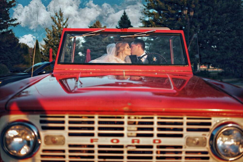 wedding photography of a couple kissing in an old ford bronco underneath a beautiful sky